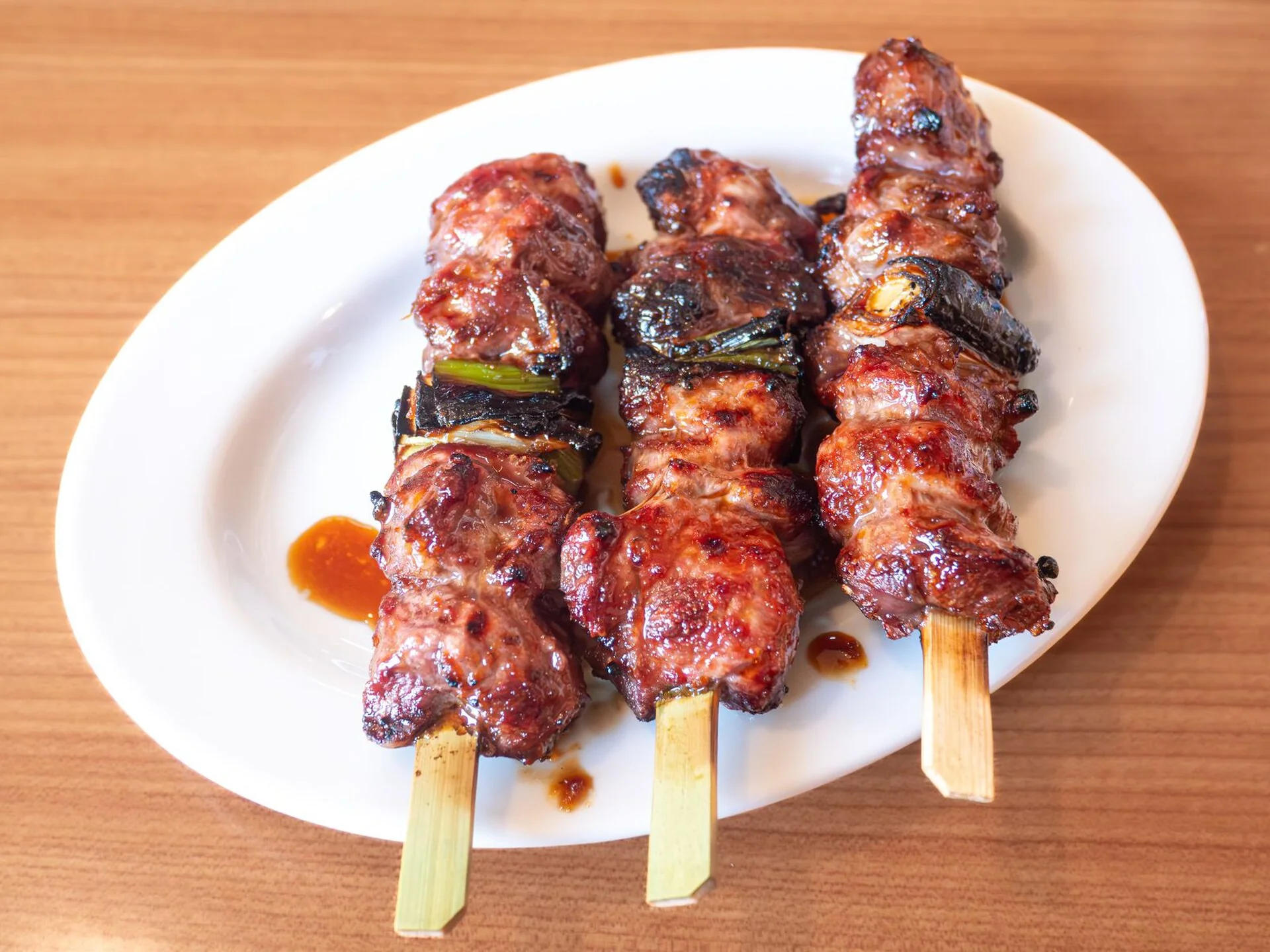 たれをまとった豚かしら肉の串焼き三本を白い皿に盛った料理