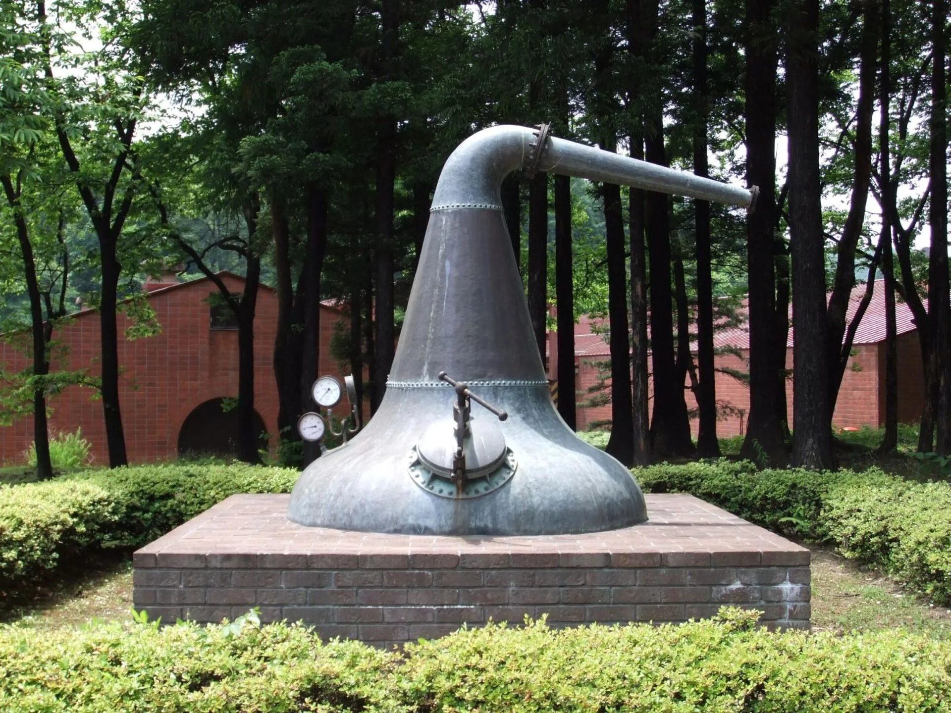 宮城峡蒸溜所の屋外に展示された蒸溜器と林、奥の建物