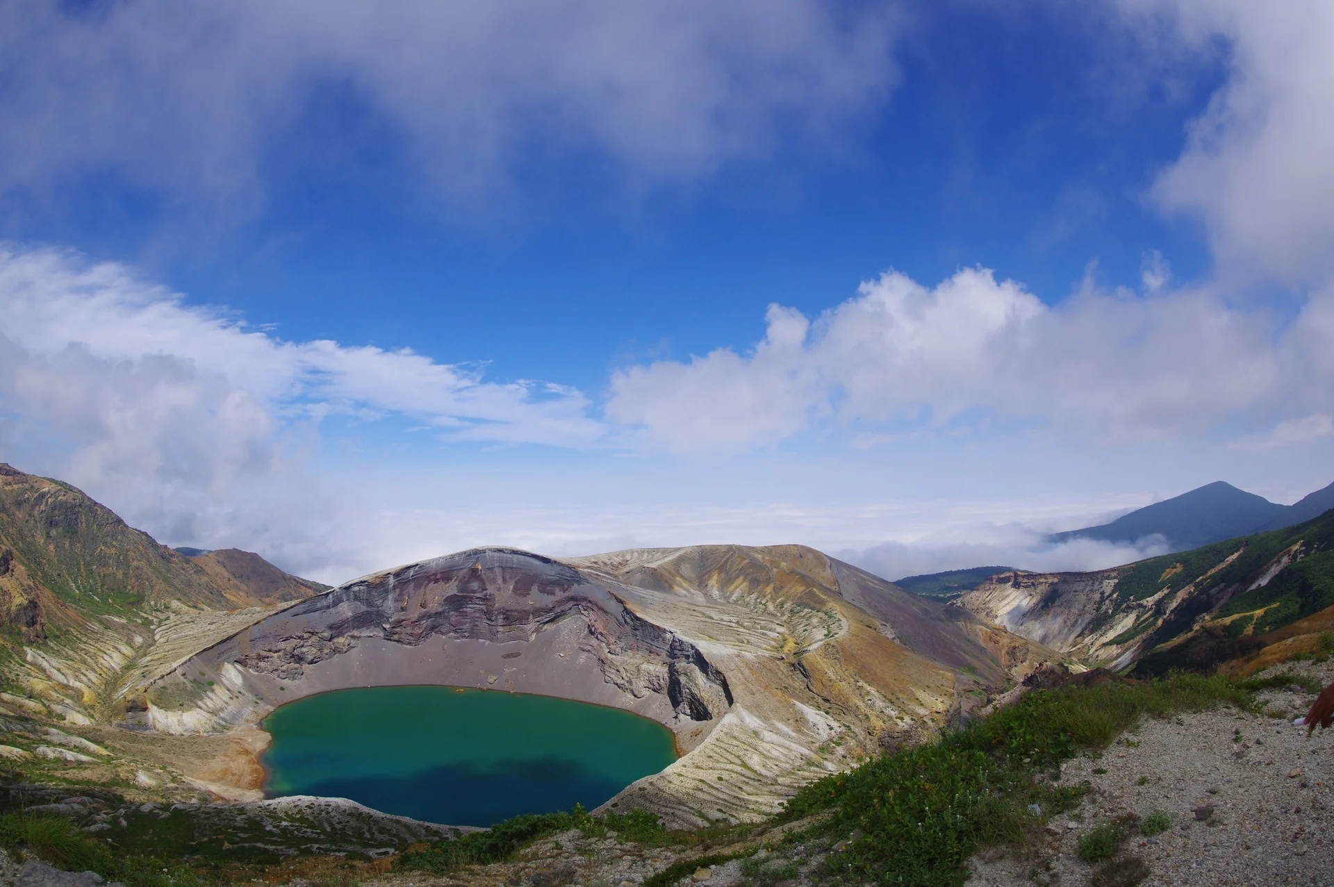 緑の火口湖と火口壁、青空を近くに見る蔵王御釜の風景